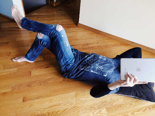 Young woman lounging on the floor with iPad in front of face